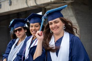 Three Goodwin University graduates smiling in blue commencement regalia.