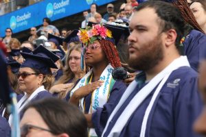 A group of graduates in blue caps and gowns standing for performances of The Star-Spangled Banner and Lift Every Voice and Sing at the Goodwin University 2025 commencement ceremony.