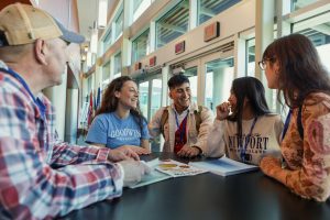 Students gather at a table in the lobby of Goodwin’s main building, talking and smiling.