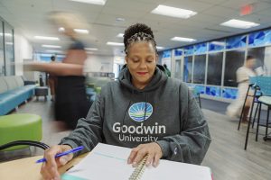 Goodwin University student looking in a notebook, with people walking in the background