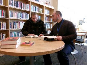A librarian and a student sit at a table with books.