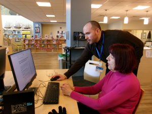 A librarian assists a student using a desktop computer.