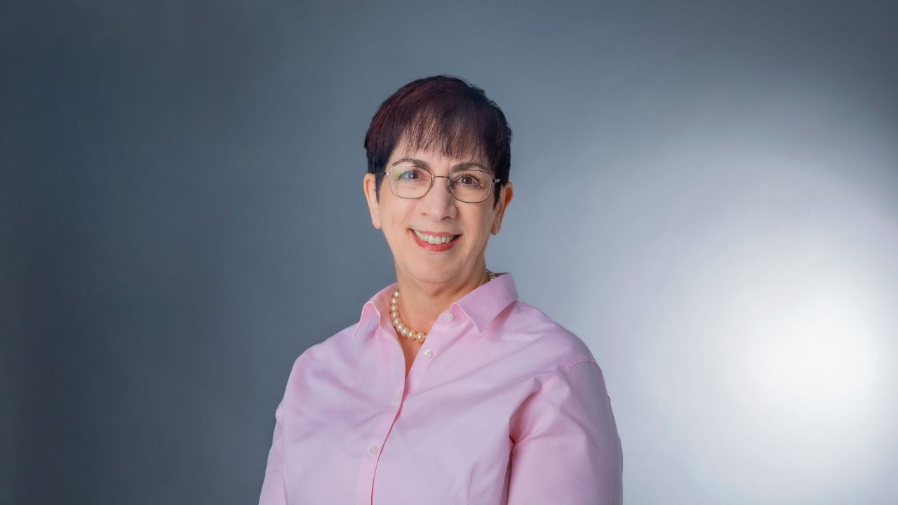 A portrait of a dark-haired woman wearing a pink shirt and glasses.