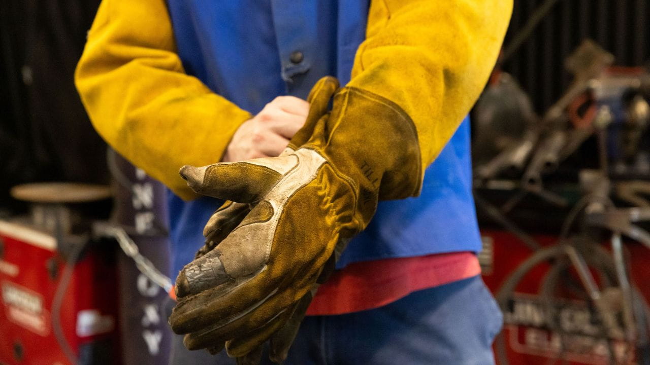A man dressed in manufacturing gear puts on a yellow glove