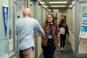 A student smiles and shakes hands with a man outside a university office.