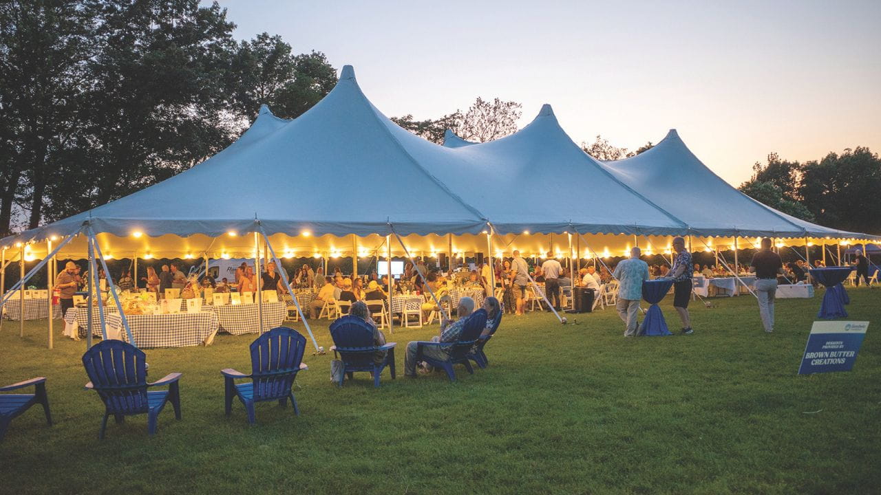A large event tent with warm lights hosts a lively gathering at dusk