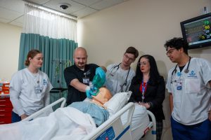 Students and an instructor watching a Hartford HealthCare employee demonstrate Ambu bag use on a manikin.