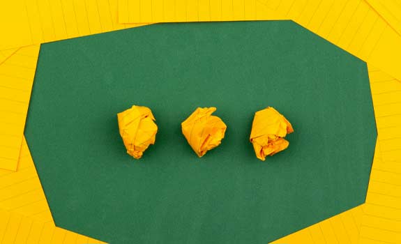 3 crumpled up pieces of paper on a table surrounded by blank notepaper