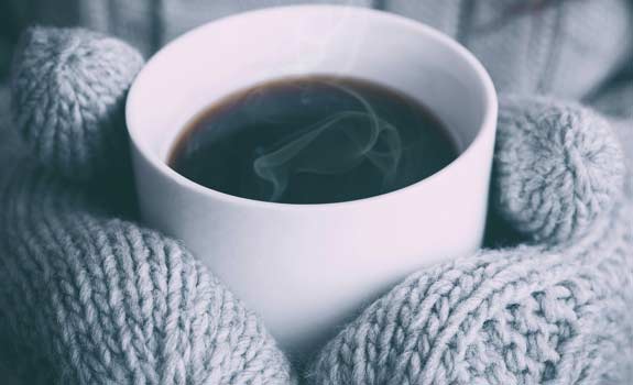 closeup of hands in mittens holding a mug of coffee