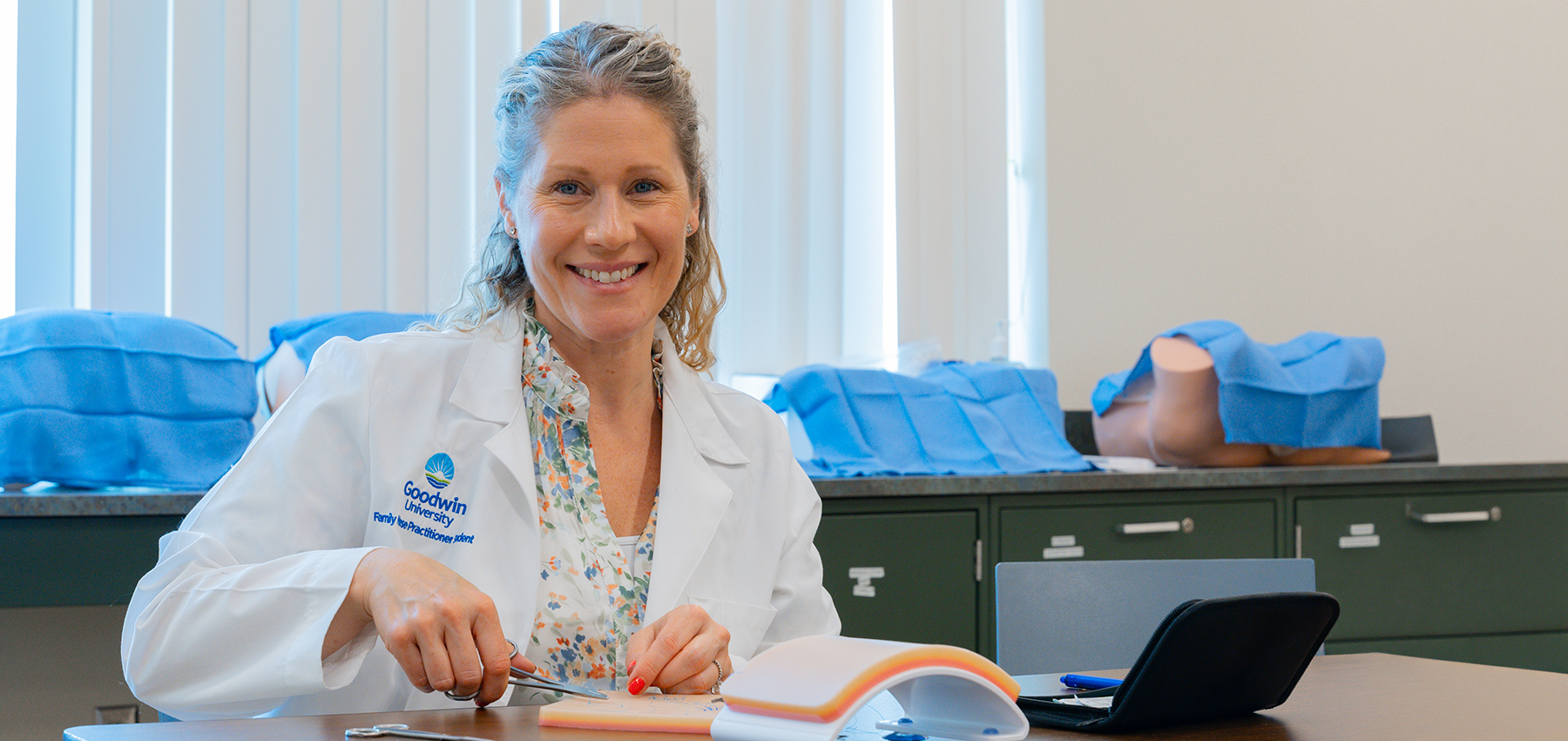 University online post-master&rsquo;s fnp and pmhnp aprn certificates student smiling while practicing stitches during a clinical lab.